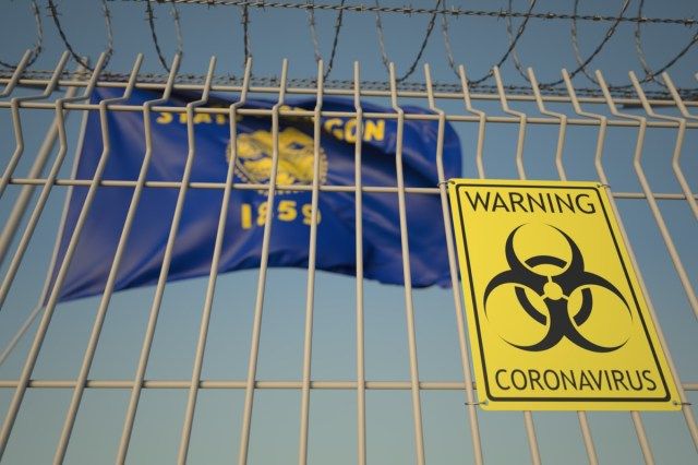 علامة Biohazard Coronavirus على سياج الأسلاك الشائكة بالقرب من علم ولاية أوريغون.'