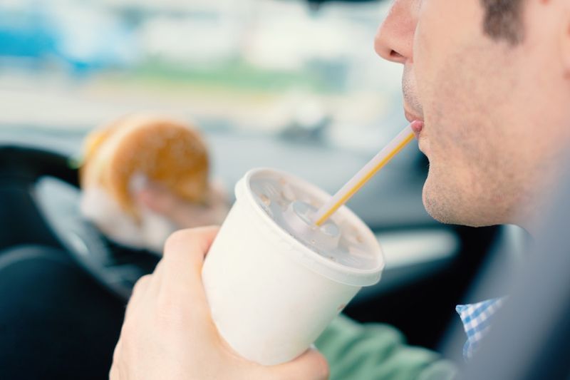 يأكل الرجل الوجبات السريعة والمشروبات الباردة بشكل خطير أثناء قيادة سيارته'