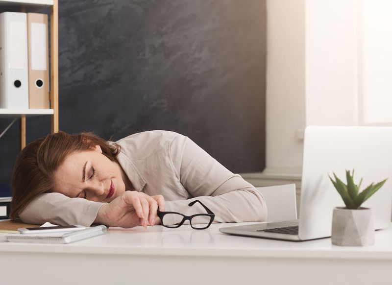 مرهقة امرأة مستلقية على مكتب في العمل'