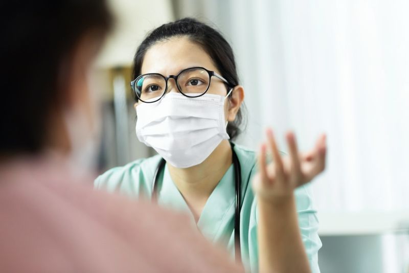 المرأة الطبيب في الزي الأخضر ارتداء النظارات والقناع الجراحي التحدث والاستشارة وتقديم المشورة للمريضة المسنة في المستشفى'