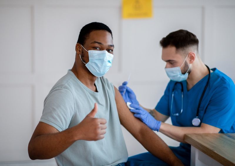 رجل أمريكي من أصل أفريقي يرتدي قناعًا مضادًا للفيروسات يشير بإبهامه أثناء التطعيم ضد فيروس كورونا ، ويوافق على التحصين ضد فيروس كورونا'