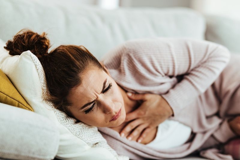 امرأة تعاني من ألم في الصدر وتسعل أثناء الاستلقاء على الأريكة في المنزل.'