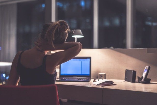 امرأة شابة منهكة ومكتئبة ومركزة تجلس في غرفتها أو مكتبها مع نوافذ فرنسية في الظلام عند المصباح'