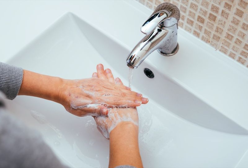 امرأة تغسل يديها بالصابون والماء في حمام المنزل'