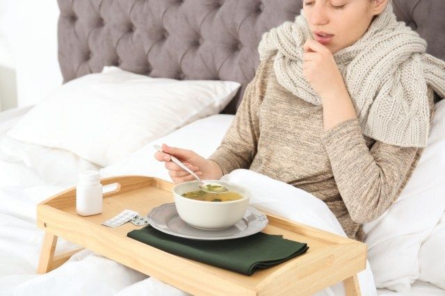 امرأة شابة مريضة تأكل المرق لعلاج البرد في الفراش في المنزل'