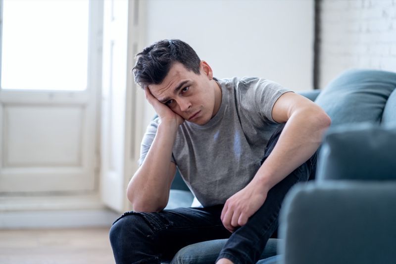 صورة لشاب يشعر بالاكتئاب واليأس يبكي وحيدًا في أريكة المنزل ويعاني من الألم العاطفي والتعاسة'