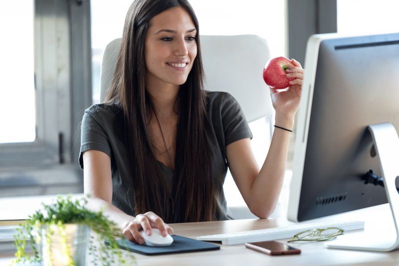 امرأة تجلس على مكتب وتأكل التفاح'