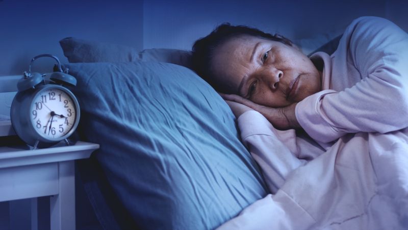 امرأة مسنة تعاني من اضطراب النوم ، تجلس في السرير تبدو حزينة'