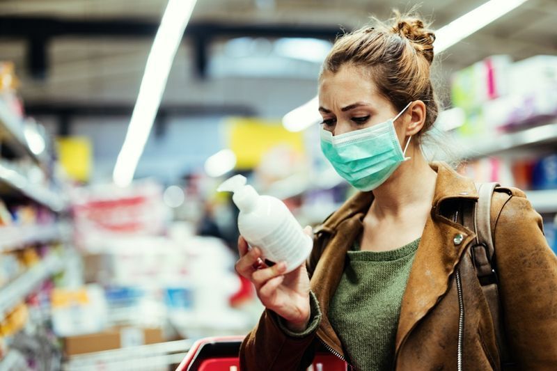 امرأة تحمل ملصق قراءة على الزجاجة قناع واقي أثناء شراء صابون اليد في السوبر ماركت أثناء وباء الفيروس'