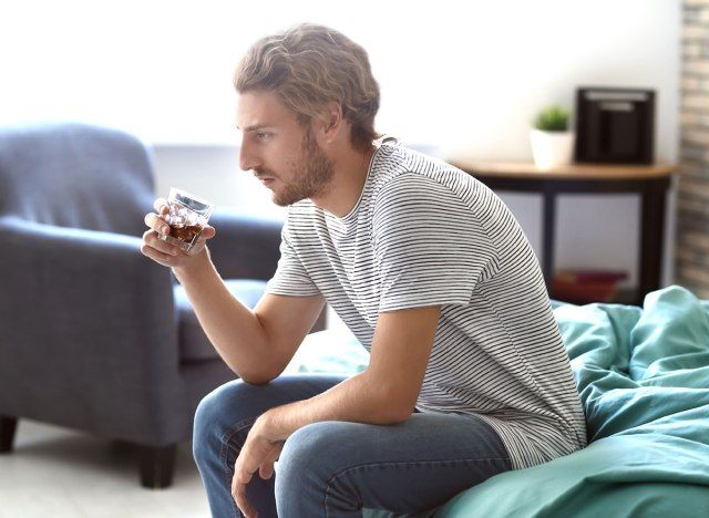 رجل جالس على السرير مع زجاج كحولي - كيف يؤثر الكحول على الدماغ'