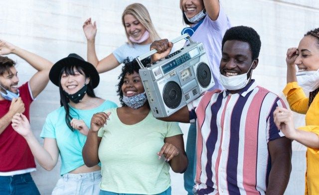 أشخاص سعداء من أعراق مختلفة يرقصون في الهواء الطلق أثناء الاستماع إلى الموسيقى من ستريو boombox القديم'