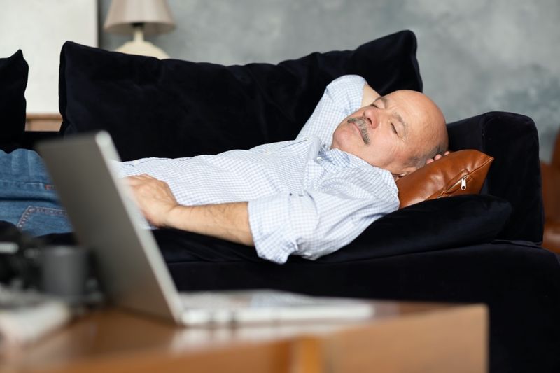 رجل كبير من أصل إسباني متعب ينام على أريكة زرقاء داكنة ، يأخذ قيلولة بعد الظهر في غرفة المعيشة'