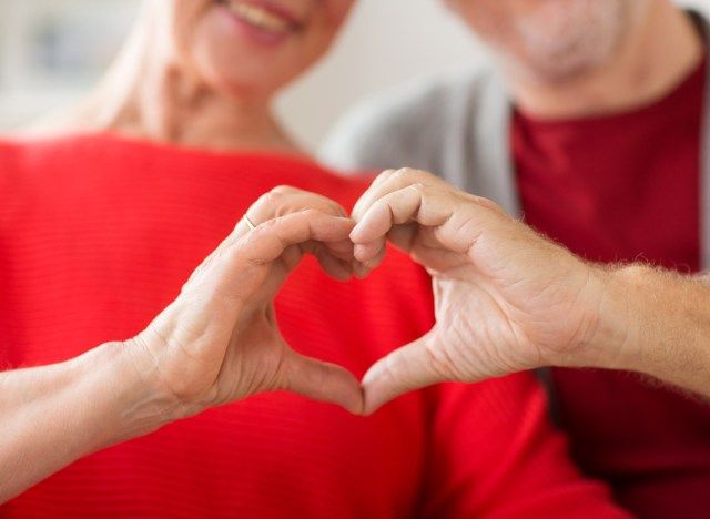 رجل وامرأة أكبر سنا يمسكان أيديهما في شكل قلب من أجل صحة قلبهما'