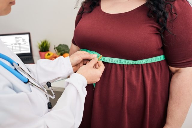   أخصائي تغذية يتفقد امرأة's waist using a meter tape
