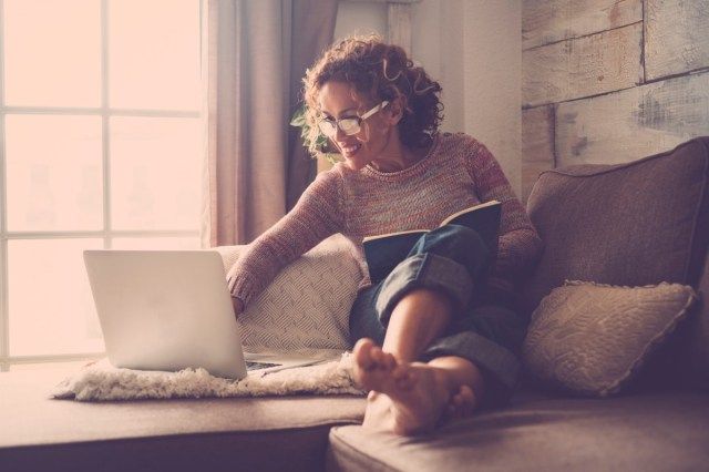امرأة في منتصف العمر تعمل في المنزل تجلس على الأريكة باستخدام جهاز كمبيوتر محمول'