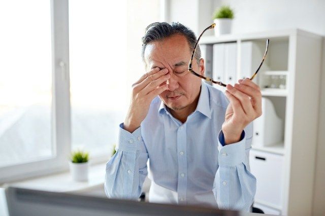 رجل أعمال متعب مع النظارات والكمبيوتر المحمول يفرك عينيه في المكتب'