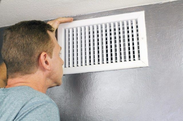 رجل يفحص شبكة وقناة تهوية الهواء الخارجة لمعرفة ما إذا كانت بحاجة إلى التنظيف'