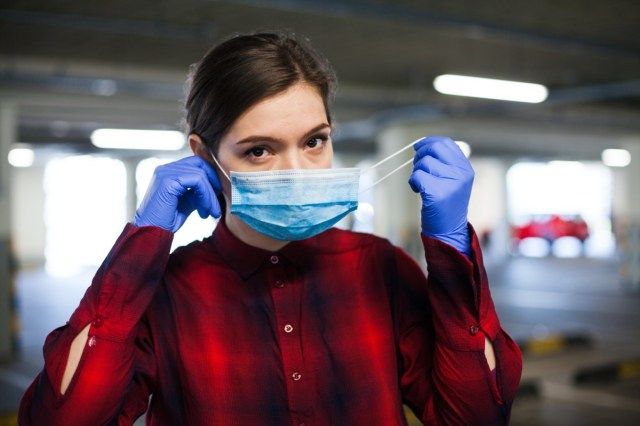 امرأة شابة من القوقاز ترتدي قفازات الجراحة وتضع قناع الوجه عليها ، وتوفر الحماية من انتشار فيروس كورونا'