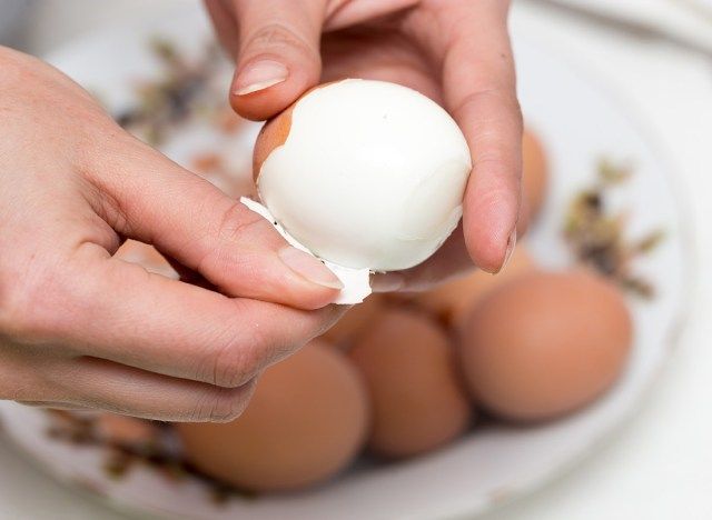 يتم تقشير البيض المسلوق باليد بسهولة فوق وعاء بيض لتقشيره'