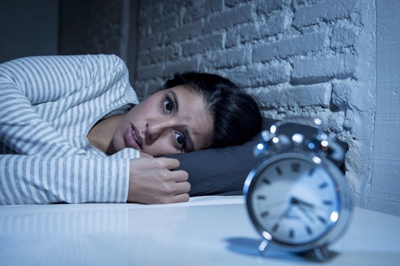 امرأة من أصل إسباني في غرفة نوم المنزل مستلقية في السرير في وقت متأخر من الليل تحاول النوم تعاني من الأرق واضطراب النوم أو خائفة من الكوابيس وتبدو حزينة وقلقة ومرهقة'