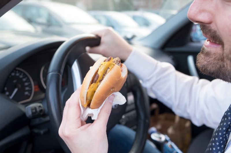 رجل يأكل هامبورجر أثناء قيادة السيارة'