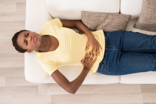 المرأة الإفريقية الشابة، الكذب على الأريكة، المعاناة من وجع المعدة'