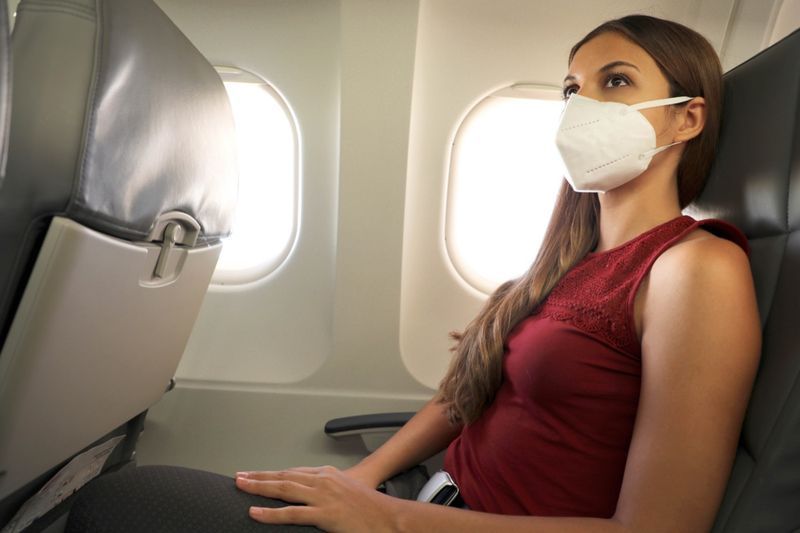 امرأة تجلس داخل طائرة ترتدي القناع الواقي KN95 FFP2'