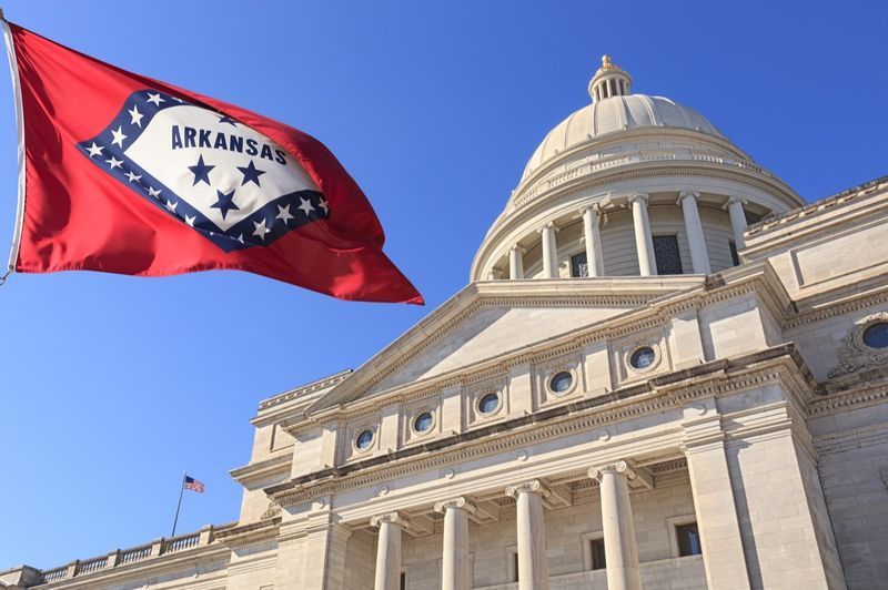 علم أركنساس يرفرف عالياً بجانب مبنى كابيتول الولاية'