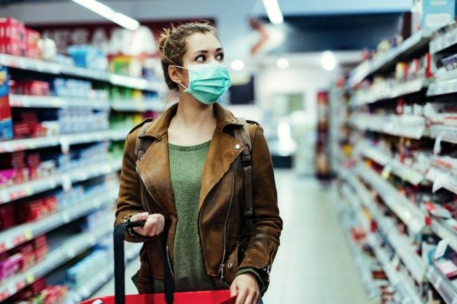امرأة شابة ترتدي قناع وجه تمشي عبر محل بقالة أثناء جائحة كوفيد -19'