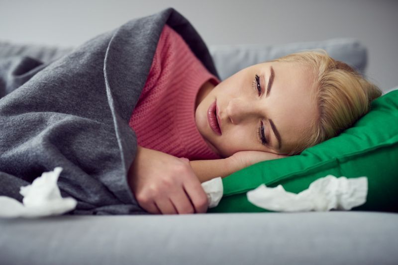 امرأة تعاني من فيروس البرد مستلقية على الأريكة تحت البطانية'