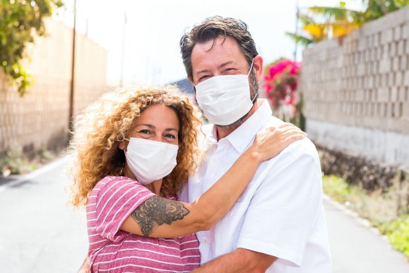 زوجان من الأشخاص السعداء في الحب يبتسمون وينظرون إلى الكاميرا وهم يرتدون قناع طبي وجراحي على الوجه للوقاية من مرض كوفيد -19 أو أي نوع من الأمراض أو الأنفلونزا'