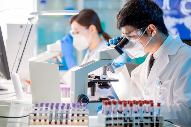 عالم الأحياء الدقيقة الآسيوي باحث في مجال التكنولوجيا الحيوية يستخدم المجهر في المختبر.'