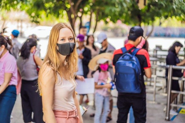 امرأة شابة ترتدي قناعًا وقائيًا للنظافة على وجهها أثناء المشي في مكان مزدحم'