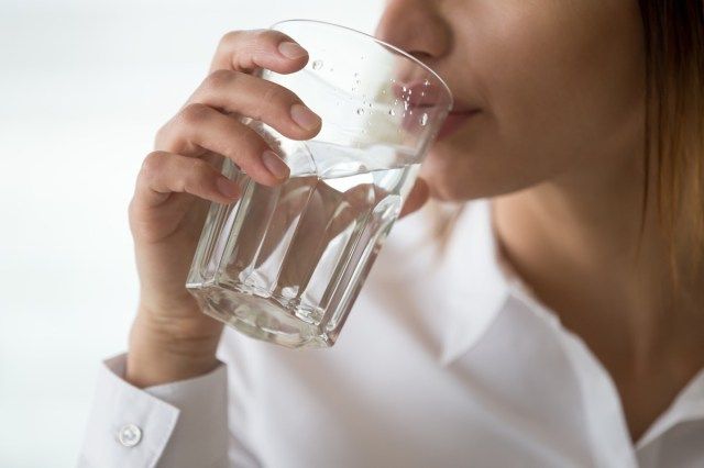 امرأة مجففة تشعر بالعطش وهي تمسك بزجاج الشرب المصفى من المياه العذبة المعدنية النقية من أجل إنعاش الجسم أو استعادة الطاقة ومشكلة الجفاف والترطيب'