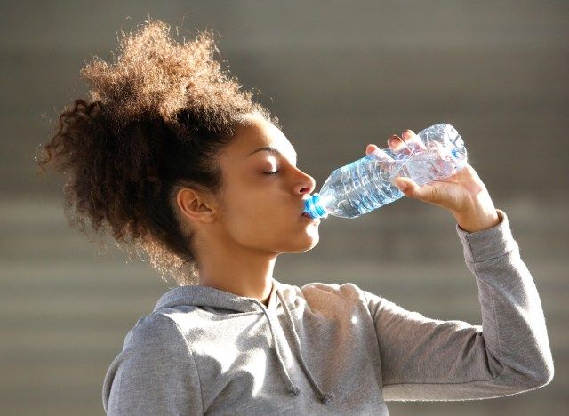 امرأة سوداء تشرب المياه المعبأة في زجاجات'