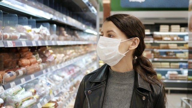 شابة تتسوق في محل بقالة للحصول على طعام وهي ترتدي قناعًا وتمنع انتشار جراثيم فيروس كورونا من خلال ارتداء قناع الوجه.'