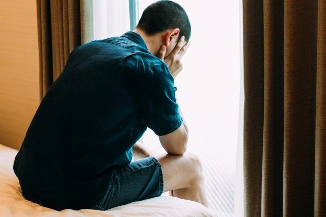رجل يعاني من الاكتئاب يجلس وحيدًا ويديه على السرير ويبكي'