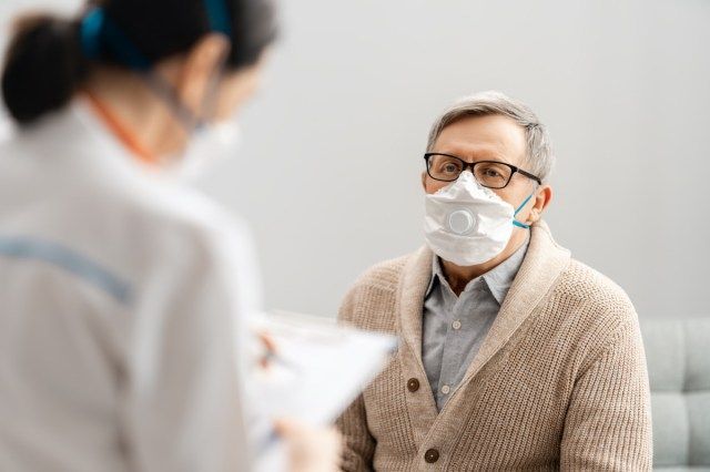 طبيب ورجل كبير يرتدون أقنعة أثناء تفشي فيروس كورونا والإنفلونزا'