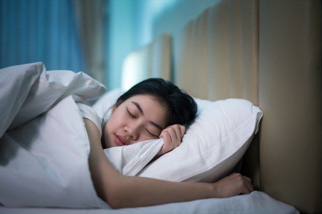 امرأة آسيوية تنام في سرير في غرفة نوم مظلمة'