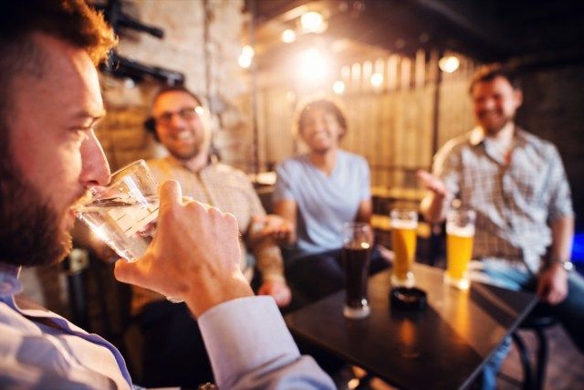 رجل يشرب كأسًا من الماء في حانة محلية بينما يضحك أصدقاؤه وهم يحتسون الجعة في المقدمة'