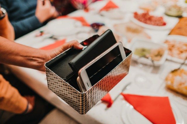 يد امرأة تحمل صندوقًا مليئًا بهواتف الضيوف الذكية في عشاءها. يأخذون استراحة مع التكنولوجيا لإجراء محادثة محببة. أسلوب الحياة.'
