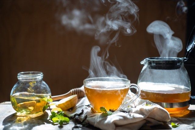 شاي ساخن في إبريق شاي زجاجي وكوب مع بخار على خلفية خشبية'