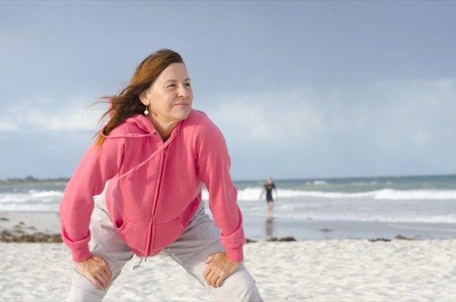 صورة لامرأة واثقة ، صحية ورياضية ، جذابة المظهر ، امرأة ناضجة في سترة وردية ، على الشاطئ ، مع غيوم عاصفة متفرقة ومحيط بري كخلفية وفضاء نسخ.'