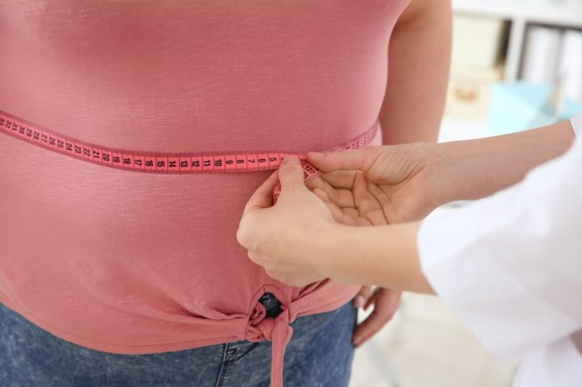   أنثى الطبيب قياس الخصر بسبب زيادة الوزن المرأة مع شريط قياس في عيادة