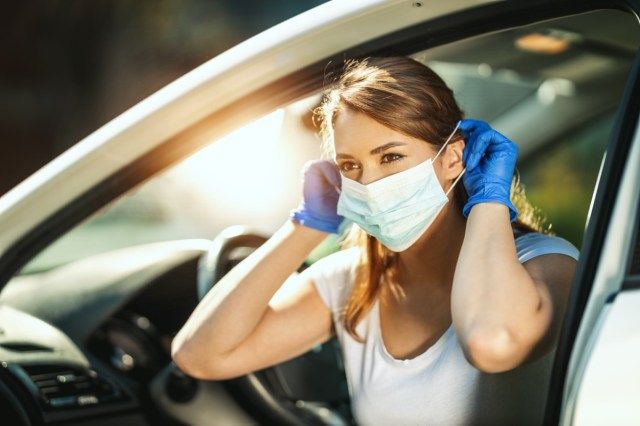 امرأة تضع قناعًا على وجهها ، لتجنب الإصابة أثناء تفشي فيروس الأنفلونزا ووباء فيروس كورونا ، والاستعداد للذهاب إلى العمل بالسيارة'
