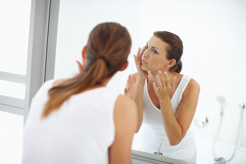 امرأة تضع المستحضر على الجلد حول عينيها في المرآة'