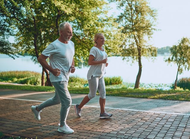   زوجان ناضجان يركضان في الهواء الطلق بجانب البحيرة ، مما يدل على عادات القلب التي تجعلك تتقدم في العمر بشكل أسرع