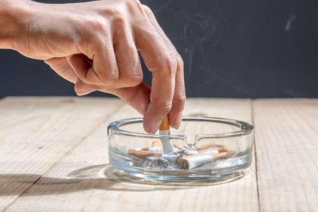   سيجارة مطوية يدويًا في منفضة سجائر شفافة على طاولة خشبية
