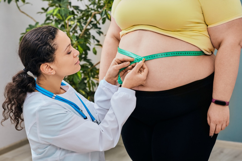   أخصائي تغذية يتفقد امرأة's waist using a measuring tape to prescribe a weight loss diet