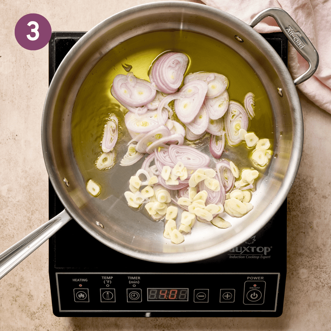 Shallots and garlic sauteing in a deep pan.
